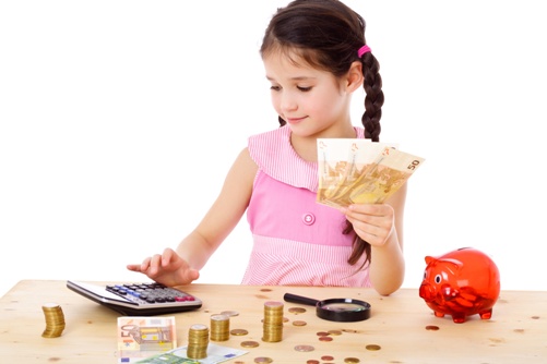 Little girl at the table counts money, isolated on white